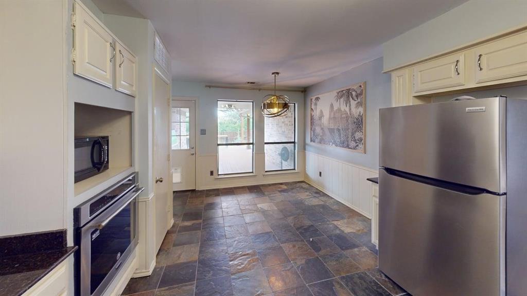 1535 Raleigh Drive Carrollton, TX 75007 - Photo 5 of 24 Kitchen and dining area featuring slate flooring, stainless steel appliances, dark countertops, white cabinetry, and a rear exterior door with glass panes