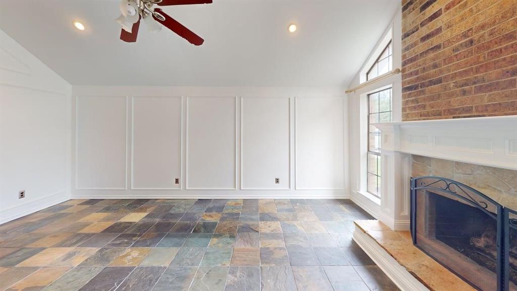 1535 Raleigh Drive Carrollton, TX 75007 - Photo 8 of 24 Spacious living area featuring multi-tone slate flooring, a brick-surround fireplace with a stone hearth and white mantel, and extensive wall paneling