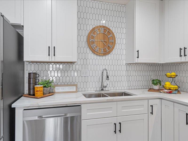 1312 Hyman Lane Austin, TX 78742 - Photo 11 of 36 The kitchen features white cabinetry with black handles, a stainless steel sink, and a white tiled backsplash