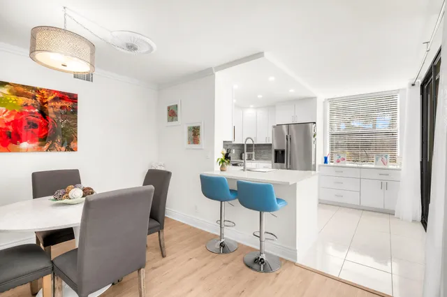 a kitchen with stainless steel appliances kitchen island granite countertop a dining table chairs and a refrigerator