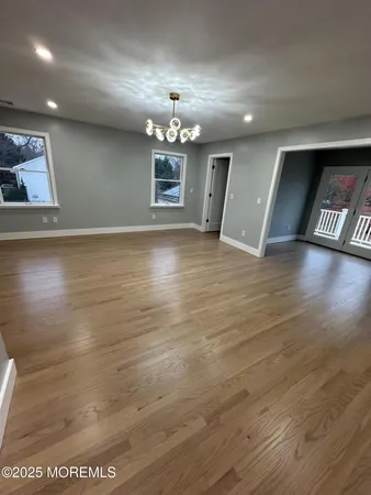 an empty room with wooden floor chandelier and windows