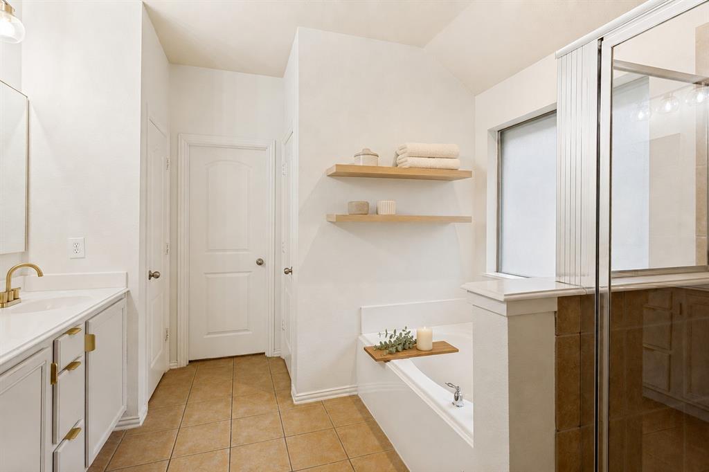 1316 Mountain Air Trail Fort Worth, TX 76131 - Photo 14 of 23 Bathroom featuring a soaking tub, glass-enclosed shower, dual vanity with brass-finish hardware, and floating shelves