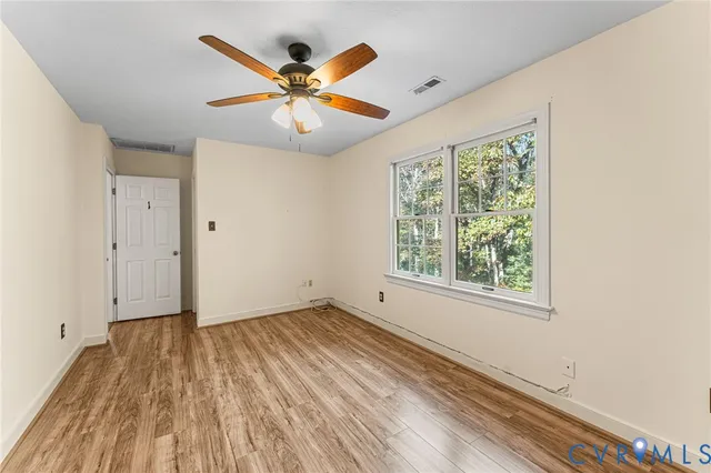 an empty room with wooden floor fan and windows