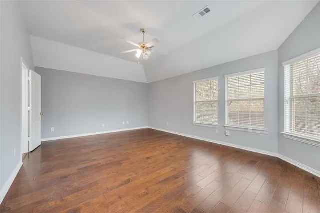 an empty room with wooden floor fan and windows