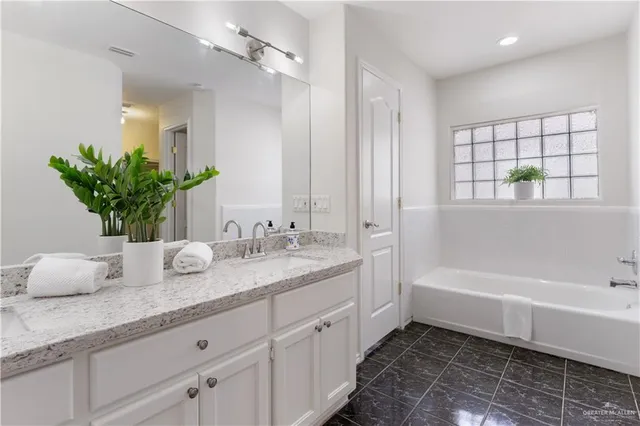 a bathroom with a granite countertop sink a large mirror a bathtub and next to a window