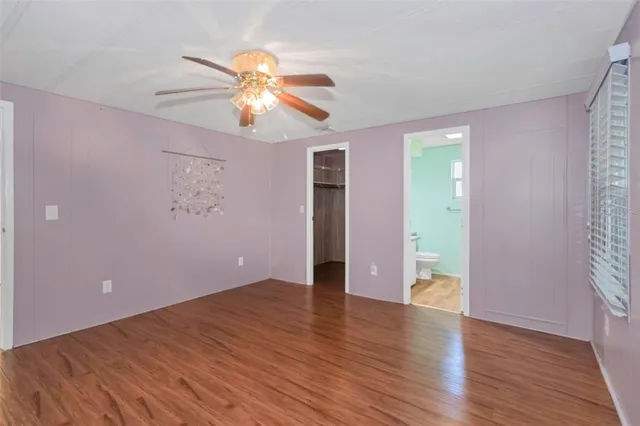 a view of an empty room with wooden floor and a ceiling fan