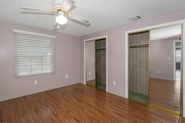 a view of an empty room with wooden floor and a ceiling fan