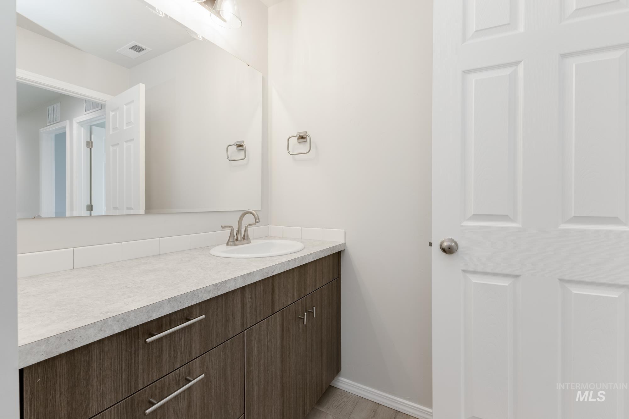 12842 Ropers Street Nampa, ID 83651 - Photo 19 of 29 Bathroom vanity featuring a wood-finish cabinet, light countertop, and an undermount sink with a brushed nickel faucet