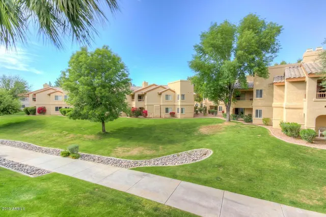 a view of a white house in front of a big yard with plants and large trees