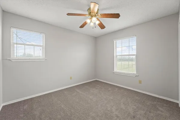 an empty room with windows and chandelier fan