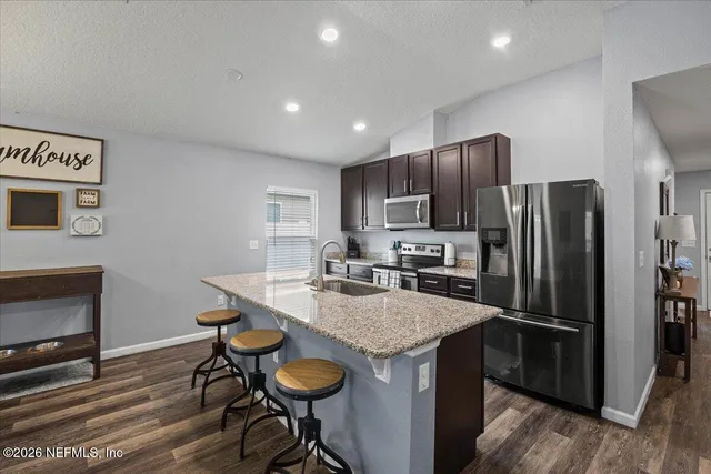 a kitchen with stainless steel appliances granite countertop a dining table chairs refrigerator and microwave