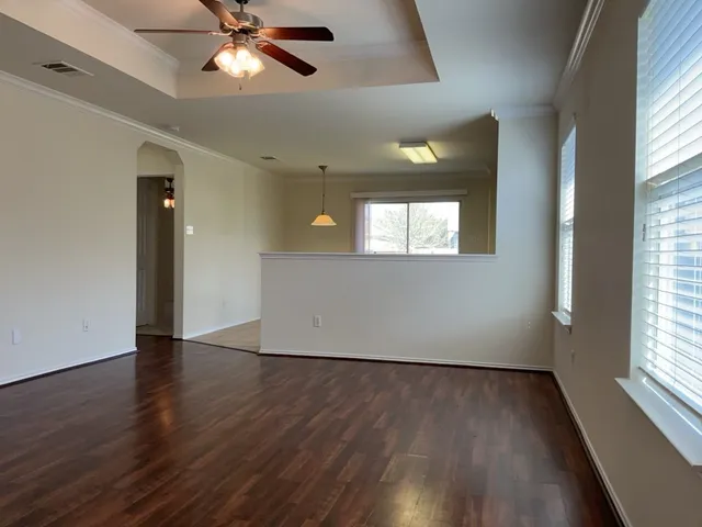 an empty room with wooden floor chandelier fan and windows
