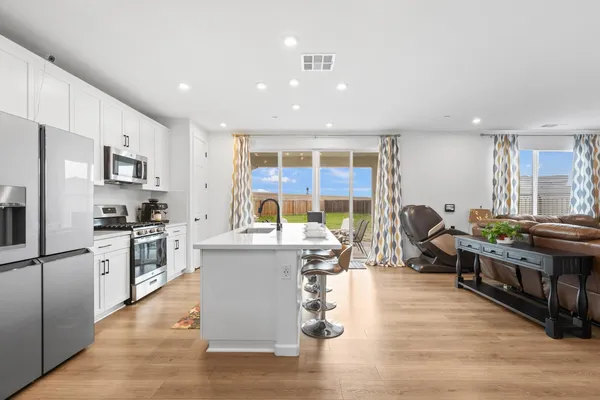 a kitchen with stainless steel appliances granite countertop a stove top oven a sink dishwasher a dining table and chairs with wooden floor