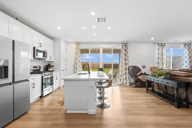 a kitchen with stainless steel appliances granite countertop a stove top oven a sink dishwasher a dining table and chairs with wooden floor