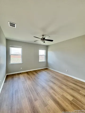 an empty room with wooden floor ceiling fan and windows