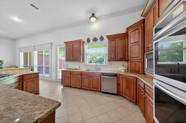 a large kitchen with stainless steel appliances granite countertop a stove top oven a sink dishwasher a dining table and chairs with wooden floor