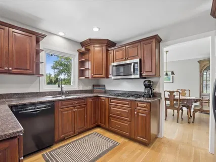 a kitchen with stainless steel appliances granite countertop a stove top oven a sink dishwasher a dining table and chairs with wooden floor