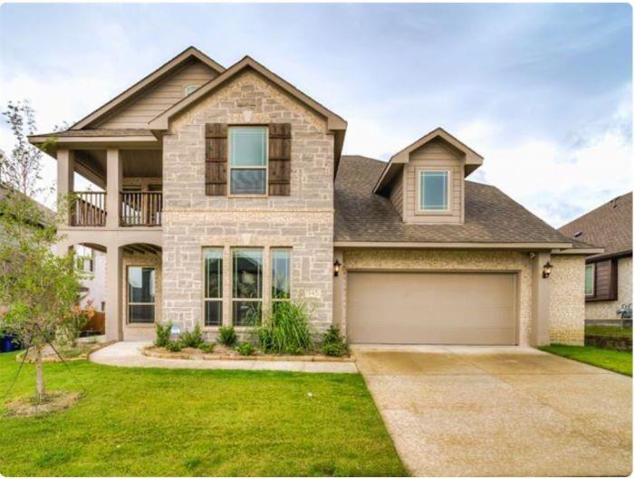 View of front of home featuring stone siding, a balcony, an attached garage, concrete driveway, and a front lawn