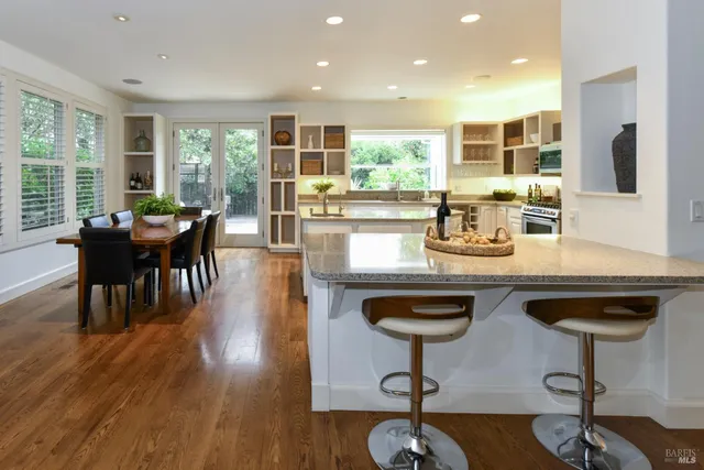 a kitchen with stainless steel appliances granite countertop a stove a refrigerator a dining table and chairs with wooden floor