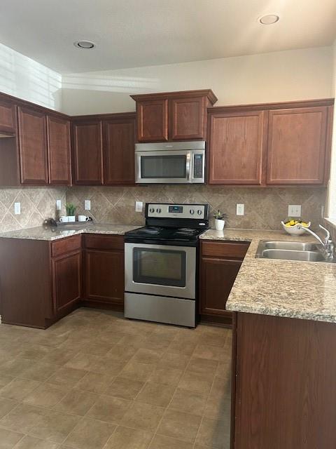 Kitchen with decorative backsplash, a sink, light stone counters, and electric stove