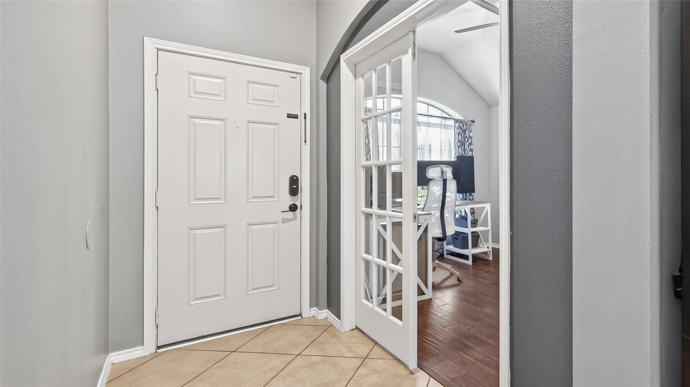 27443 Rebecca Field Lane Spring, TX 77386 - Photo 4 of 31 This photo showcases a welcoming entryway with a white front door and tiled flooring. Adjacent are elegant French doors leading to a bright office space with wood flooring and an arched window, offering a modern and functional layout.