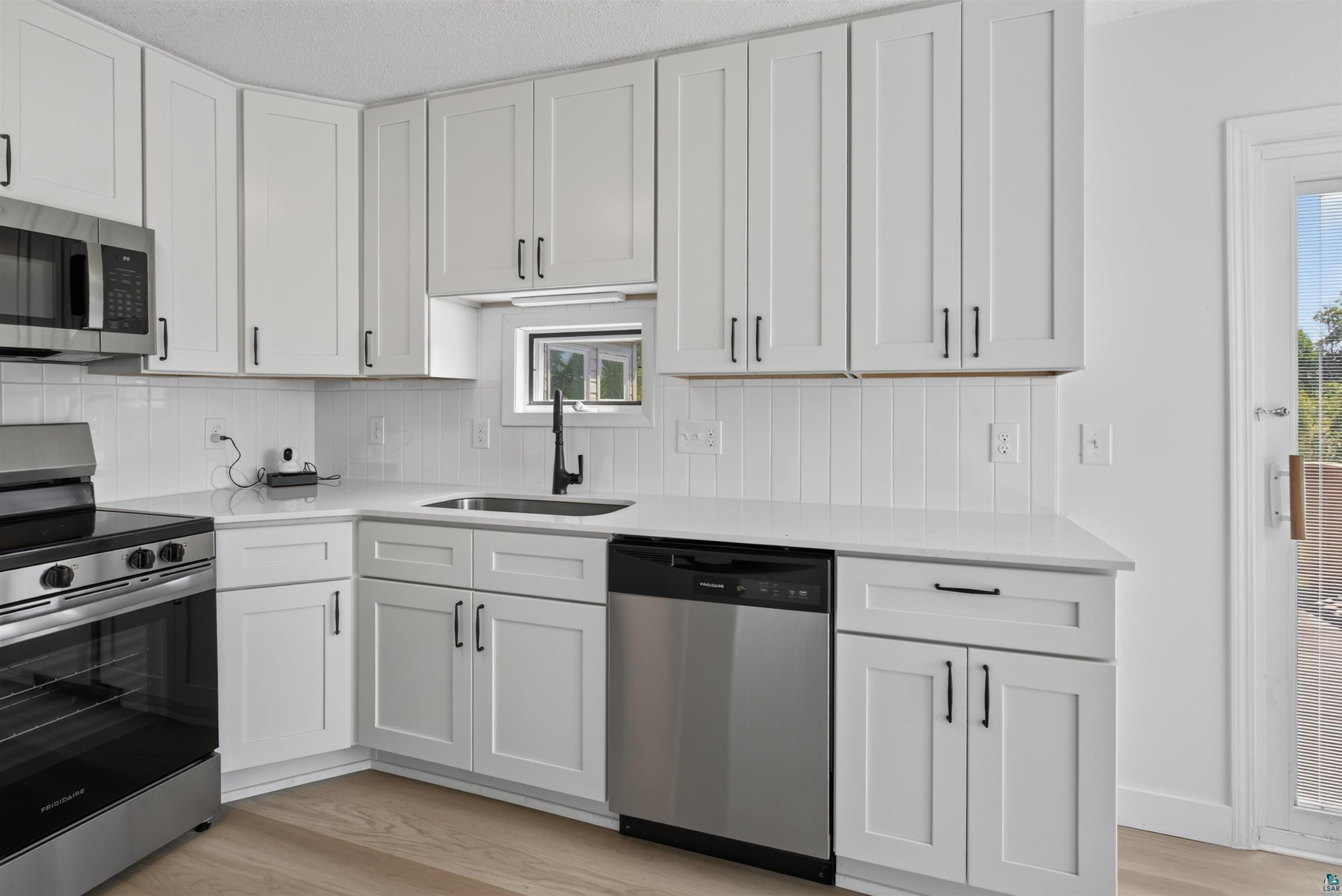 5868 Rice Lake Road Duluth, MN 55803 - Photo 15 of 39 Modern kitchen featuring white shaker-style cabinetry, stainless steel appliances, white subway tile backsplash, light-toned wood-finish flooring, and a glass-paneled exterior door