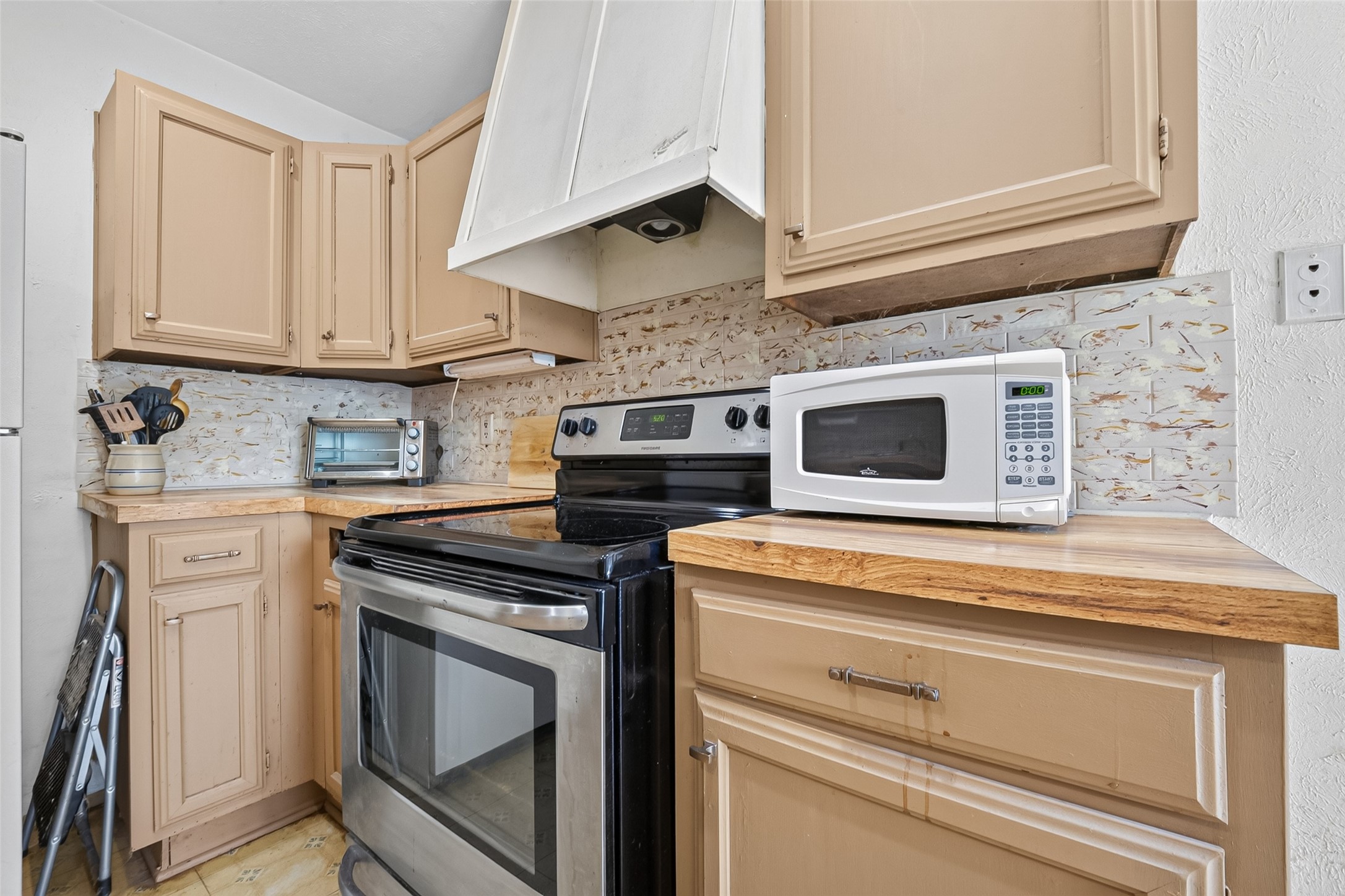22926 Millgate Drive Spring, TX 77373 - Photo 12 of 34 Cozy kitchen with warm-toned cabinets, wood countertops, and modern appliances, including a microwave and stove. The space features a unique tile backsplash and offers ample storage.