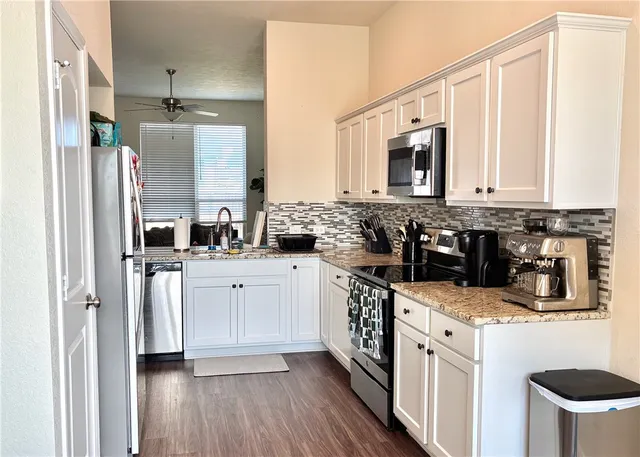 a kitchen with stainless steel appliances kitchen island granite countertop a refrigerator a stove a sink and white cabinets