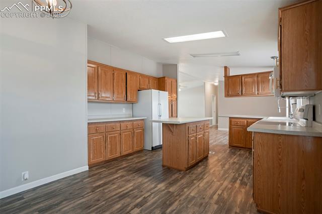 20150 Enoch Road Colorado Springs, CO 80928 - Photo 15 of 50 Kitchen with white appliances, a center island, brown cabinets, dark wood-style flooring, and baseboards
