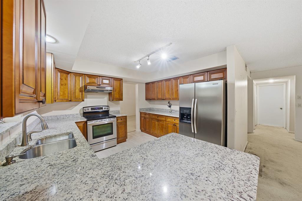 a kitchen with stainless steel appliances kitchen island granite countertop a refrigerator a sink a stove with island cabinets and wooden floor