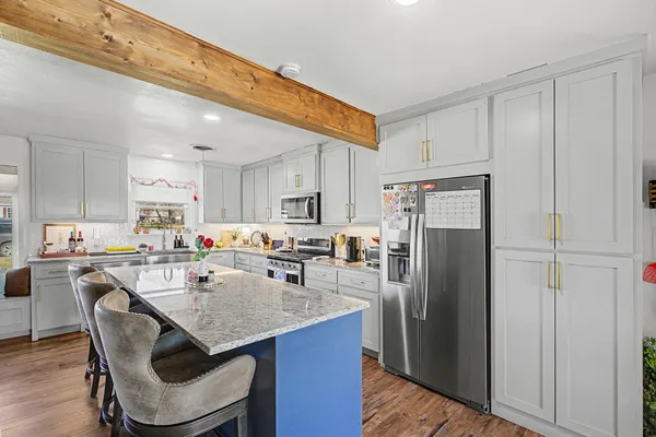 a kitchen with stainless steel appliances granite countertop a dining table chairs refrigerator and cabinets