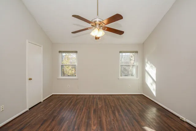an empty room with wooden floor fan and windows