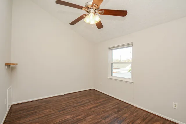 an empty room with wooden floor fan and windows
