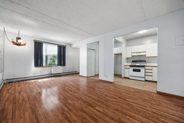 a view of empty room with wooden floor and kitchen