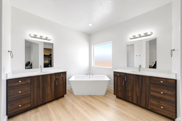 5963 Flattop Drive St. George, UT 84790 - Photo 22 of 45 Spacious bathroom featuring a freestanding soaking tub, dual wood-finish vanities with white countertops, light wood-finish flooring, and natural light from a rectangular window