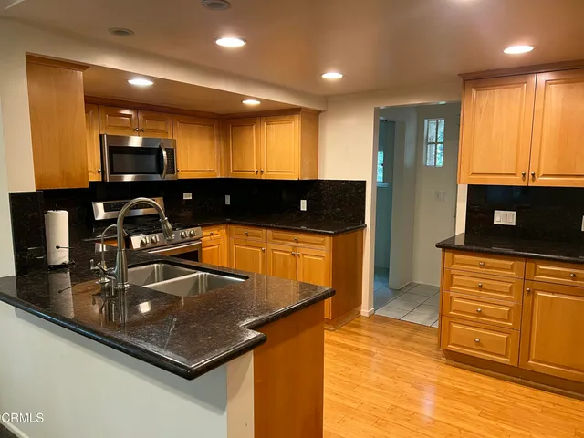 a kitchen with stainless steel appliances a sink a stove a microwave a counter top and living room view