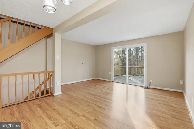 a view of an empty room with wooden floor and fan