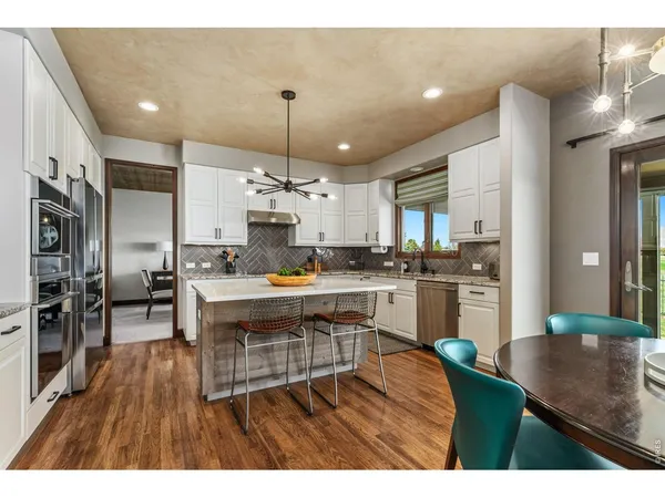 a kitchen with stainless steel appliances kitchen island granite countertop a refrigerator a stove a sink dishwasher a dining table and chairs with wooden floor