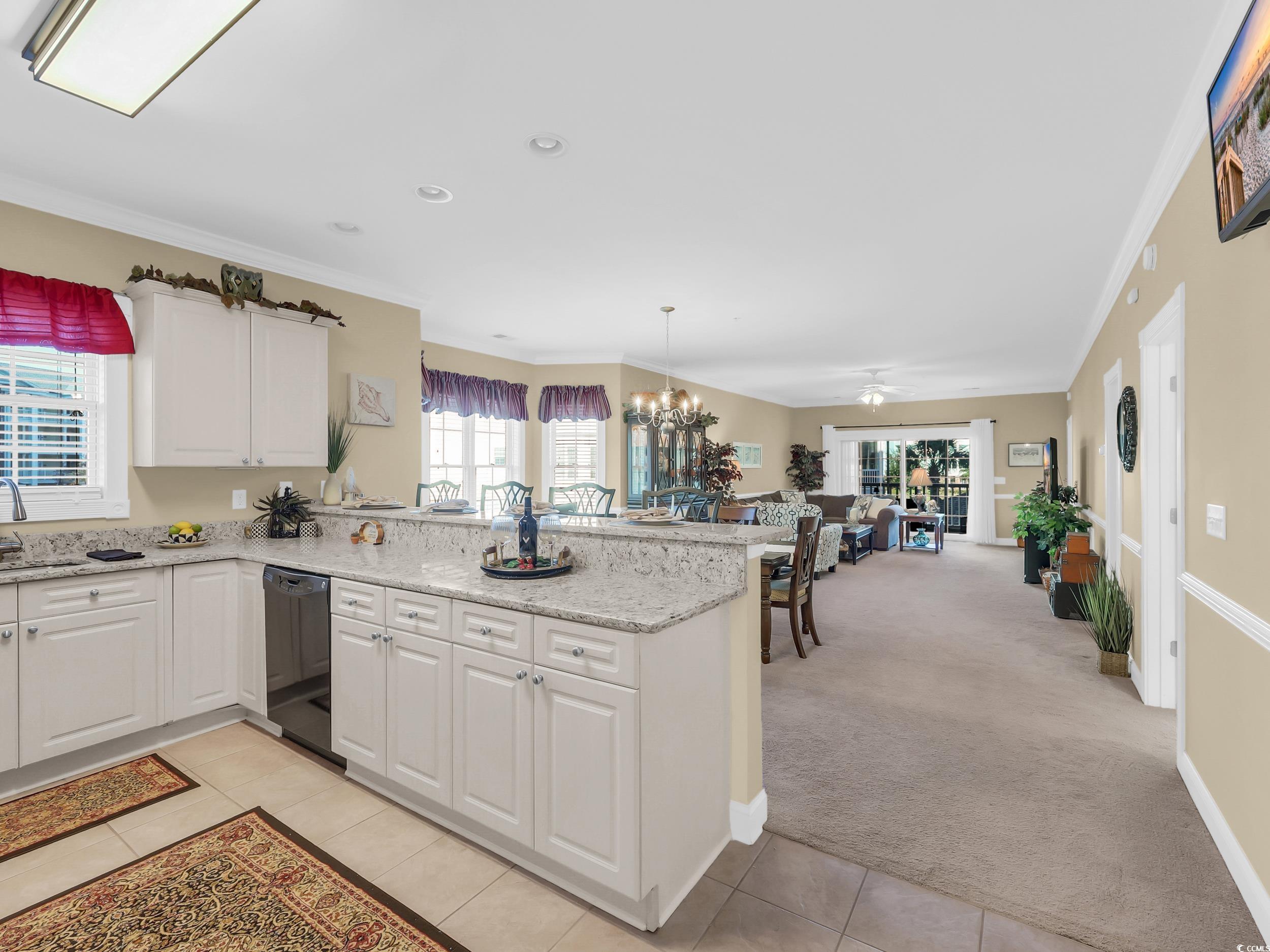 4833 Luster Leaf Circle, Unit 201 Myrtle Beach, SC 29577 - Photo 10 of 39 Kitchen with light colored carpet, white cabinetry, crown molding, a peninsula, and light stone counters