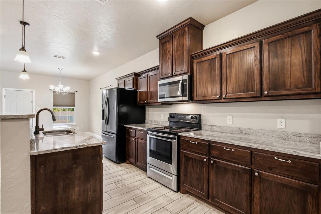 1502 Reed Street Greenville, TX 75401 - Photo 11 of 26 Kitchen featuring dark wood cabinetry, light granite countertops, and stainless steel appliances