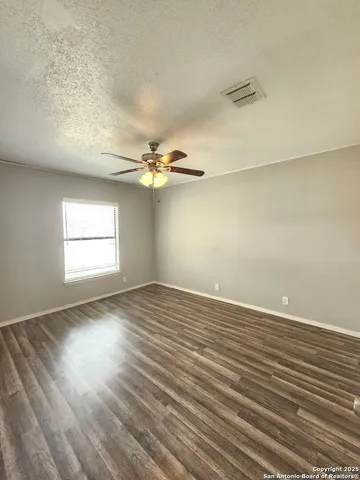 an empty room with wooden floor chandelier fan and windows