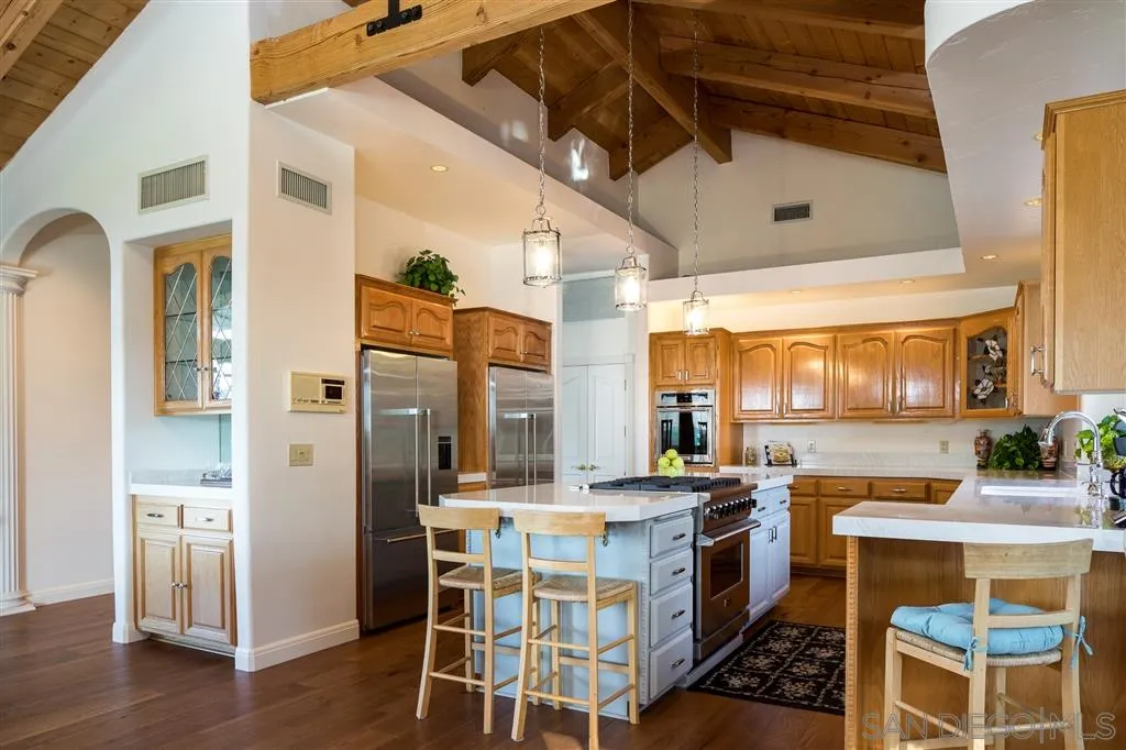 12966 Lomas Verdes Drive Poway, CA 92064 - Photo 11 of 25 a kitchen with stainless steel appliances kitchen island granite countertop a table chairs in it and wooden floors