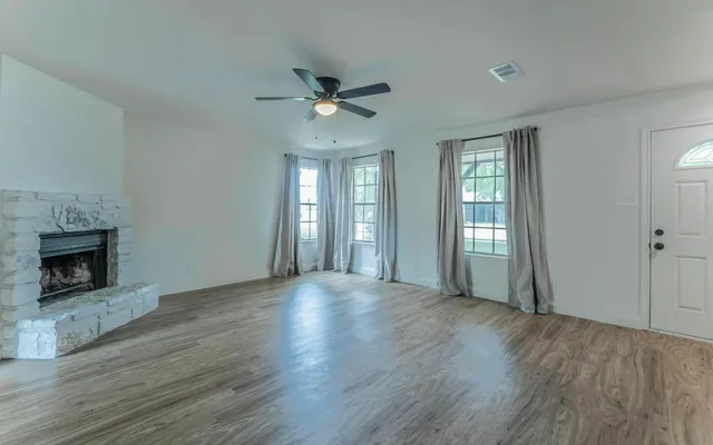 an empty room with wooden floor fireplace and windows