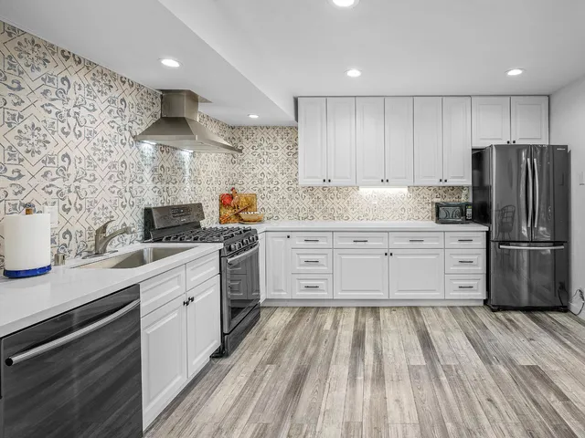 a kitchen with stainless steel appliances a sink dishwasher a refrigerator and white cabinets with wooden floor