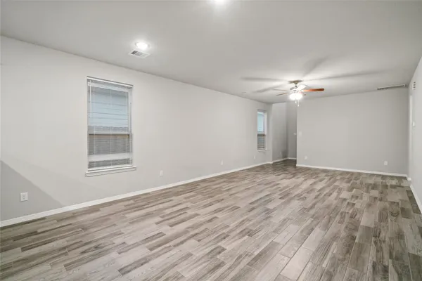 a view of an empty room with wooden floor and fan