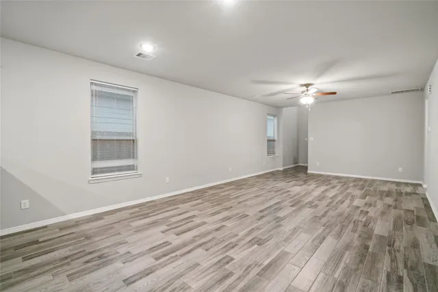 a view of an empty room with wooden floor and fan