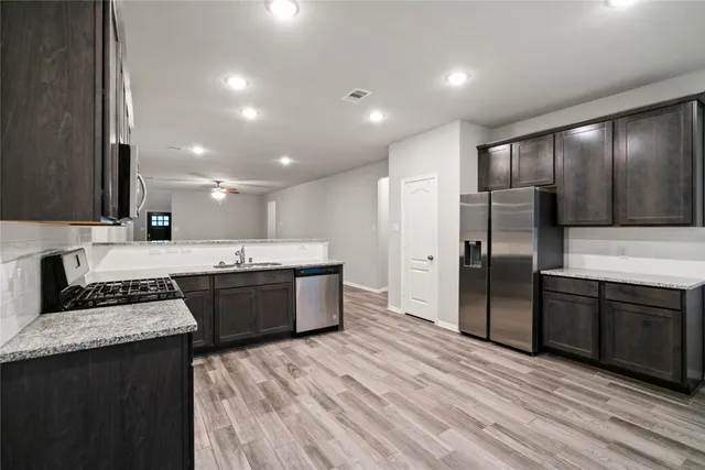 a large kitchen with stainless steel appliances granite countertop a stove a sink dishwasher a refrigerator and white cabinets with wooden floor