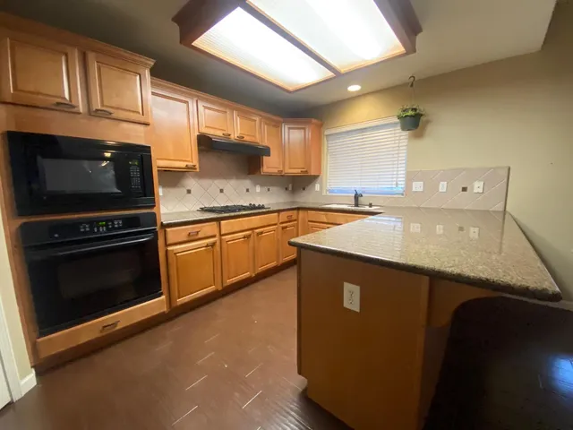 a kitchen with granite countertop a sink a stove top oven and cabinetry