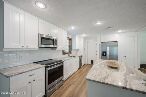 a large kitchen with granite countertop white cabinets and stainless steel appliances