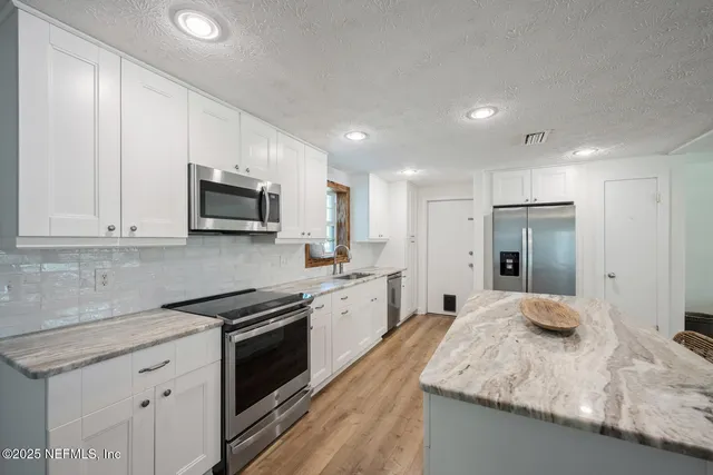 a large kitchen with granite countertop white cabinets and stainless steel appliances